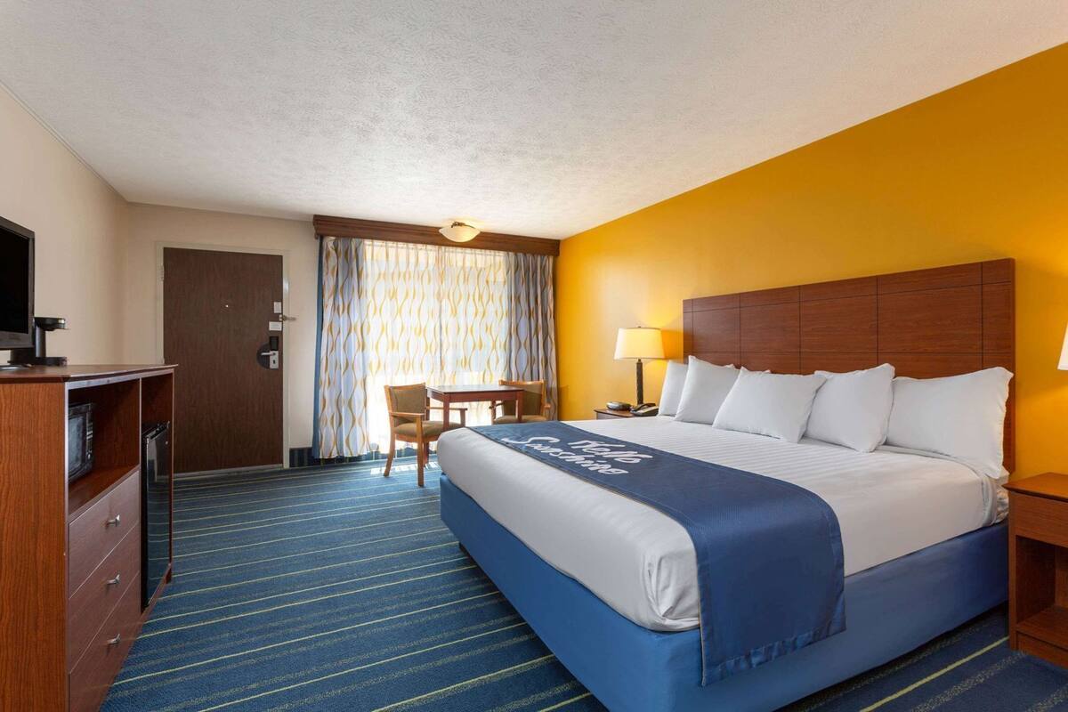 Una habitación de hotel con cama, escritorio, silla, televisor y lámpara.