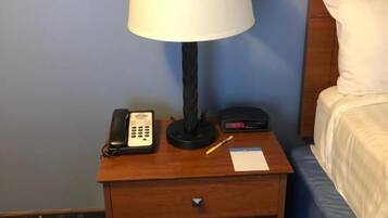 Une table de chevet en bois, avec une lampe blanche, un téléphone et une horloge numérique.
