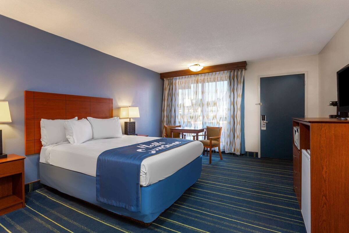 Habitación de hotel con cama, escritorio, silla, televisor y puerta.