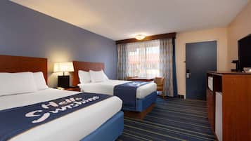A hotel room with two beds, a desk, a chair, a television, and a door.
