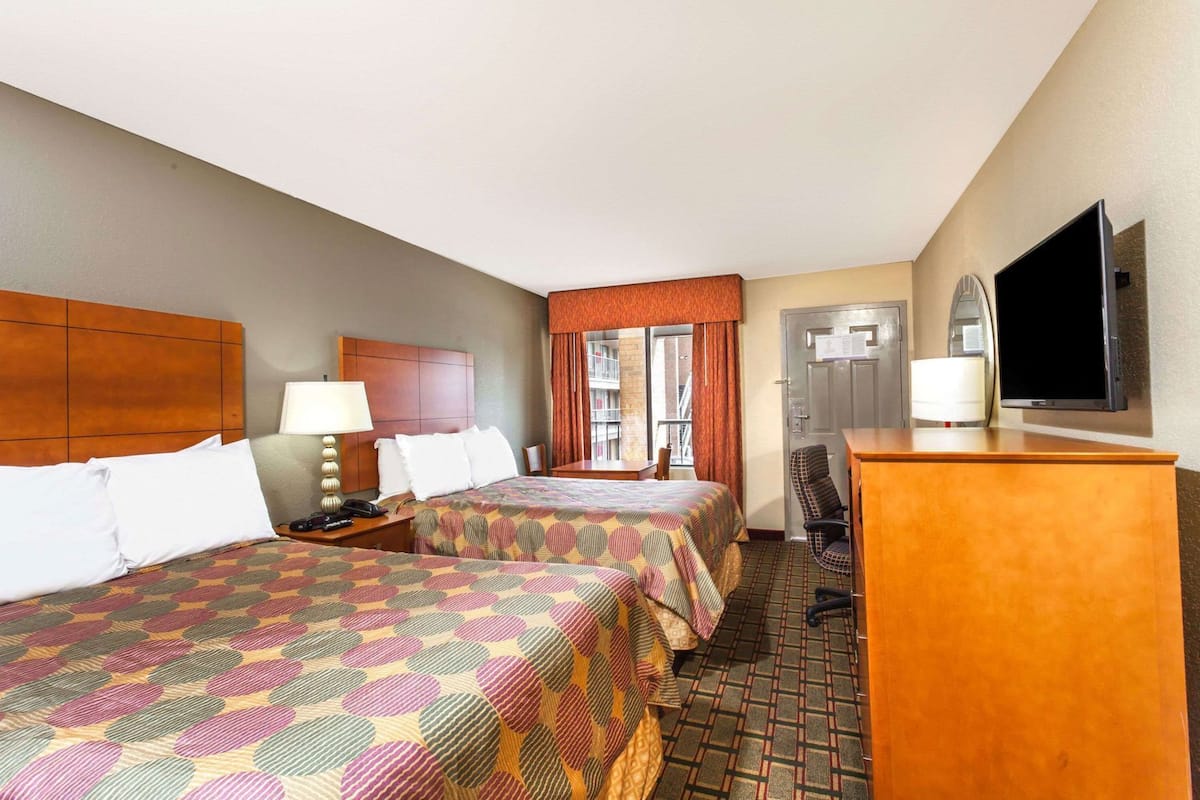 A hotel room with two beds, a desk, a television, and a window with a view.