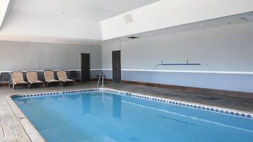 Una piscina interna con bordo piastrellato, una scala e diverse sedie lungo la parete.