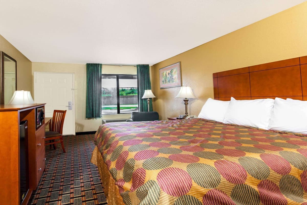 A hotel room with a bed, a desk, a chair, a lamp, and a window with curtains.
