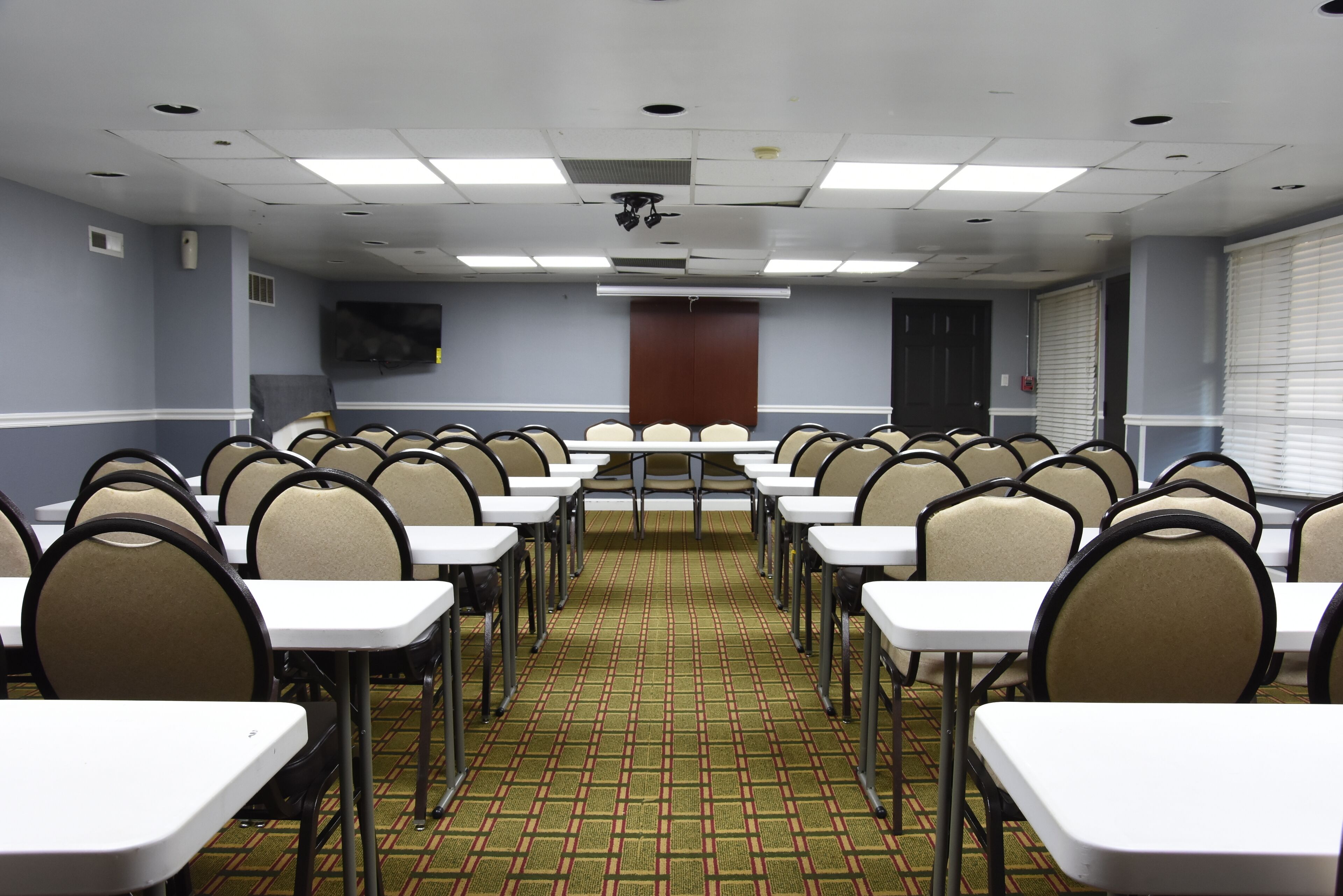 A conference room with rows of tables and chairs, a projector screen, and a patterned carpet.