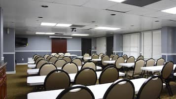 A conference room with multiple tables and chairs, a flat-screen TV mounted on the wall, and a door in the background.