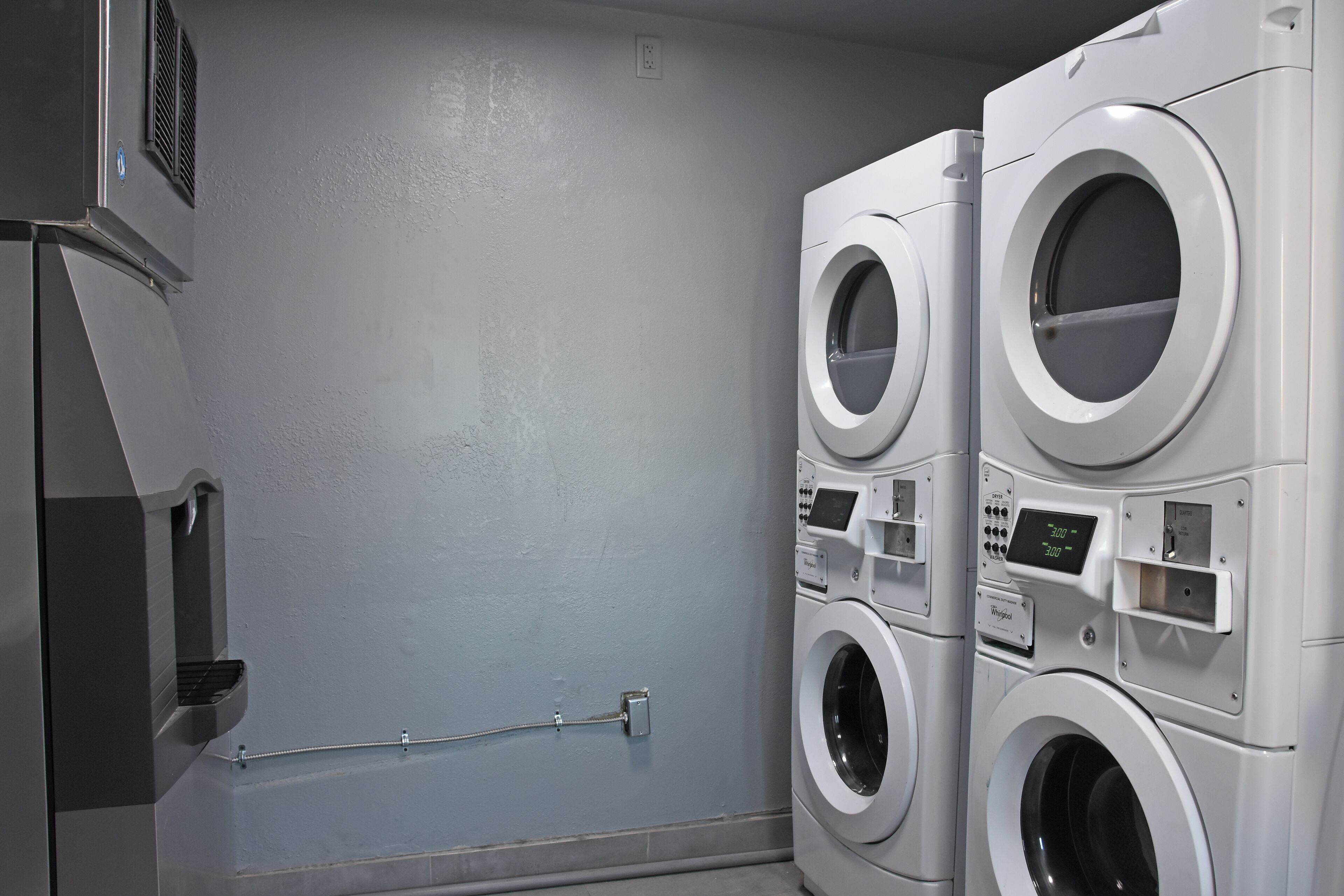 Une buanderie équipée de deux machines à laver à chargement frontal superposées et d’un sèche-linge fixé au mur.