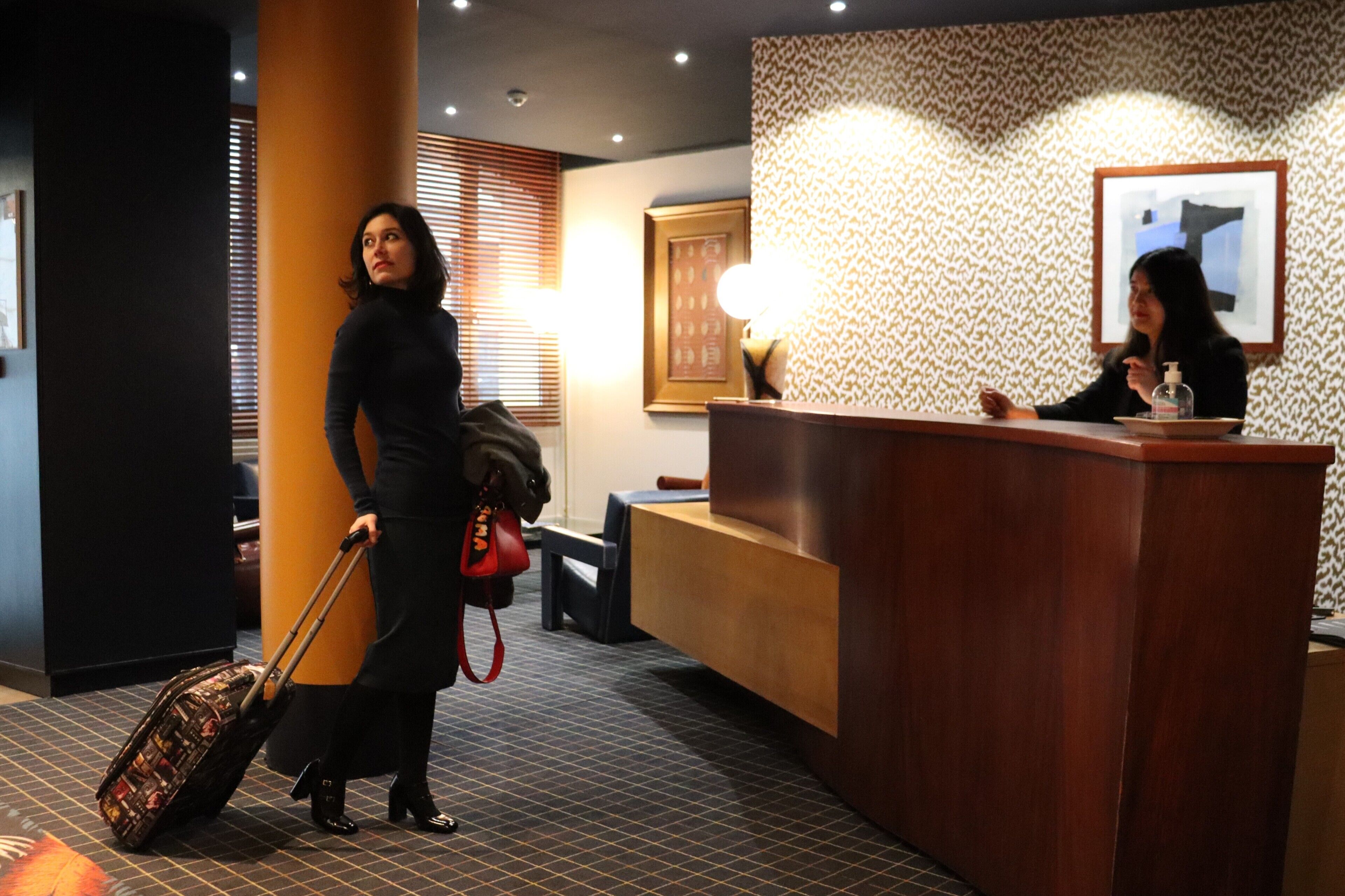 Un espace d’accueil d’hôtel comprenant un comptoir de réception, un espace d’attente avec un banc et une grande colonne.