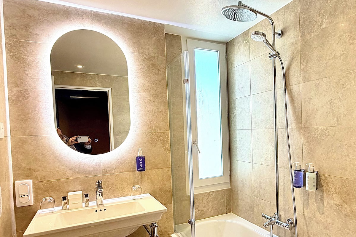 Un baño moderno con un espejo grande, un lavamanos, una bañera y una ducha.