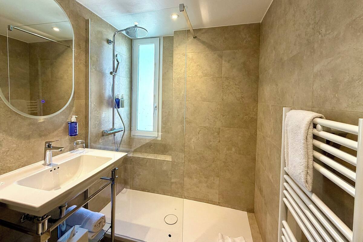 Un baño con ducha, lavamanos, espejo y barra para toallas.
