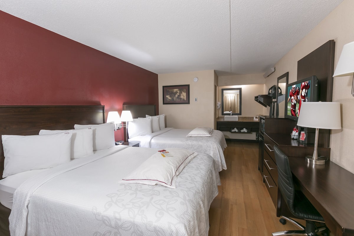 A hotel room with two beds, a desk, a chair, a lamp, and a mirror.