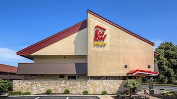 Stylish hotel building with a flat roof and red overhang, set amidst landscaped greenery and a parking lot.
