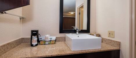 A bathroom with a granite countertop, a white sink, a black coffee maker, and a mirror with a black frame.