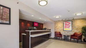 A reception area with a counter, a Red Roof Plus sign, and two chairs. - Red Roof Inn PLUS+ Boston - Framingham (Framingham)