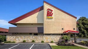 A Red Roof Plus hotel with a stone facade, a parking lot, and a clear blue sky. - Red Roof Inn PLUS+ Boston - Framingham (Framingham)