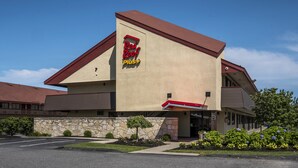 A Red Roof Plus hotel with a stone facade, a red roof, and a landscaped front yard. - Red Roof Inn PLUS+ Boston - Framingham (Framingham)