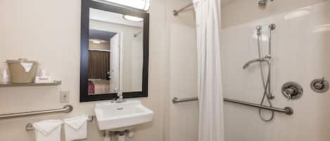 Un baño con lavamanos, espejo, ducha y barras de apoyo.