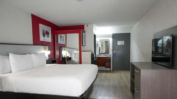 A hotel room with a large bed, a TV, a desk, and a bathroom visible through an open door. - Ramada by Wyndham Tulsa Broken Arrow (Broken Arrow)