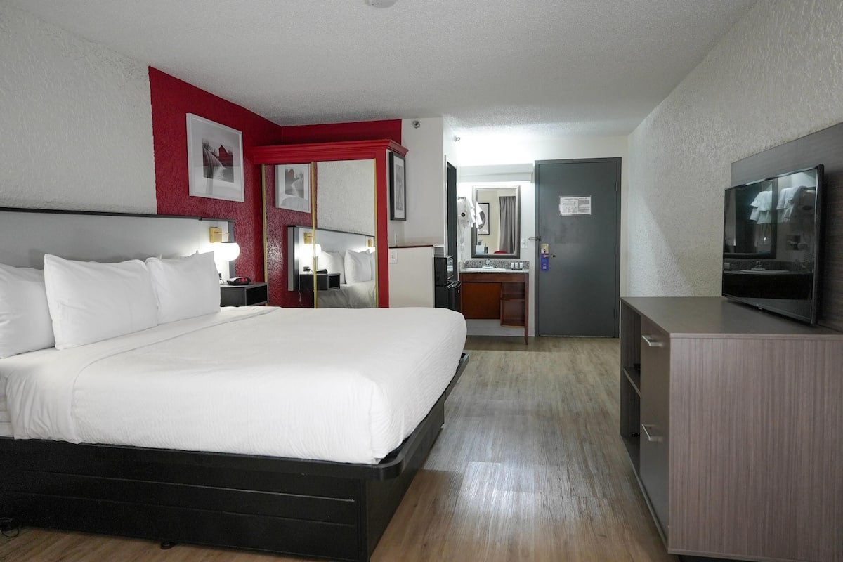 Habitación de hotel con una cama grande, televisión, escritorio y baño visible a través de una puerta abierta.