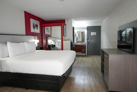 A hotel room with a large bed, a TV, a desk, and a bathroom visible through an open door.