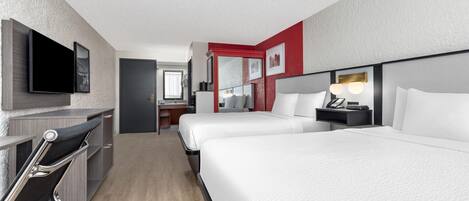 A hotel room with two beds, a desk, a chair, a TV, and a bathroom visible in the background.