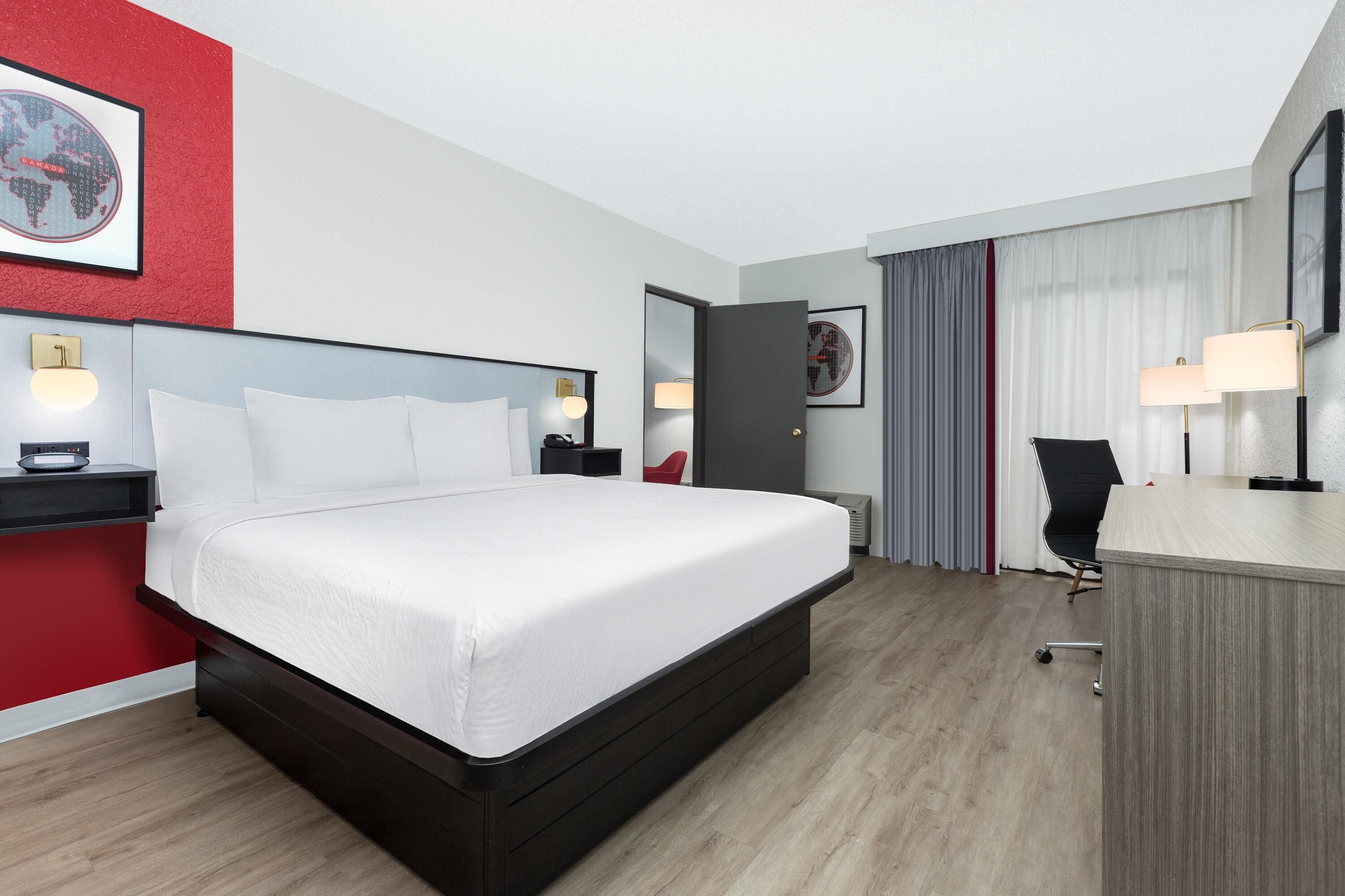 A hotel room with a large bed, bedside tables, a desk with a chair, and a red accent wall.