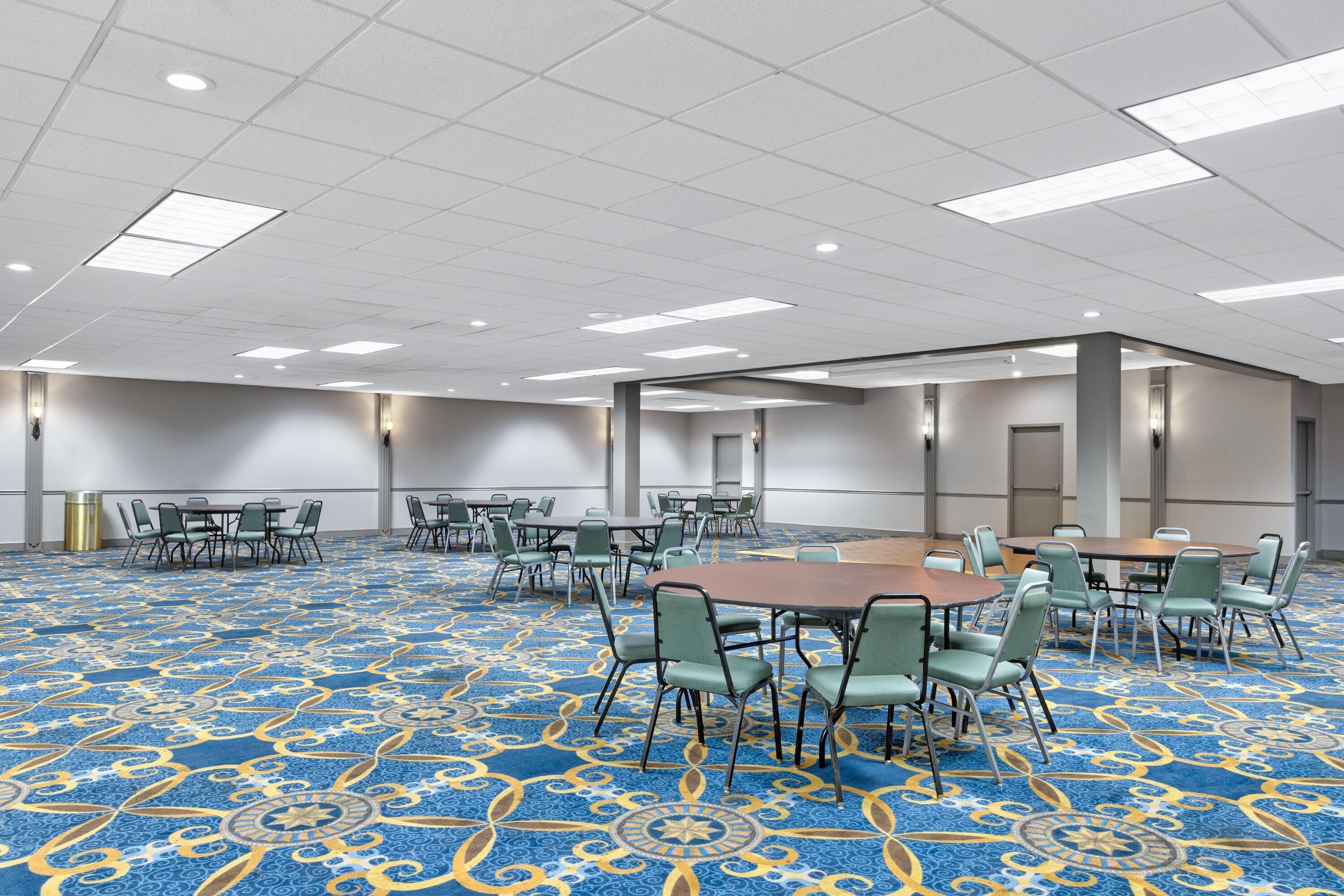 A conference room with tables and chairs, a patterned carpet, and a white ceiling with lights.