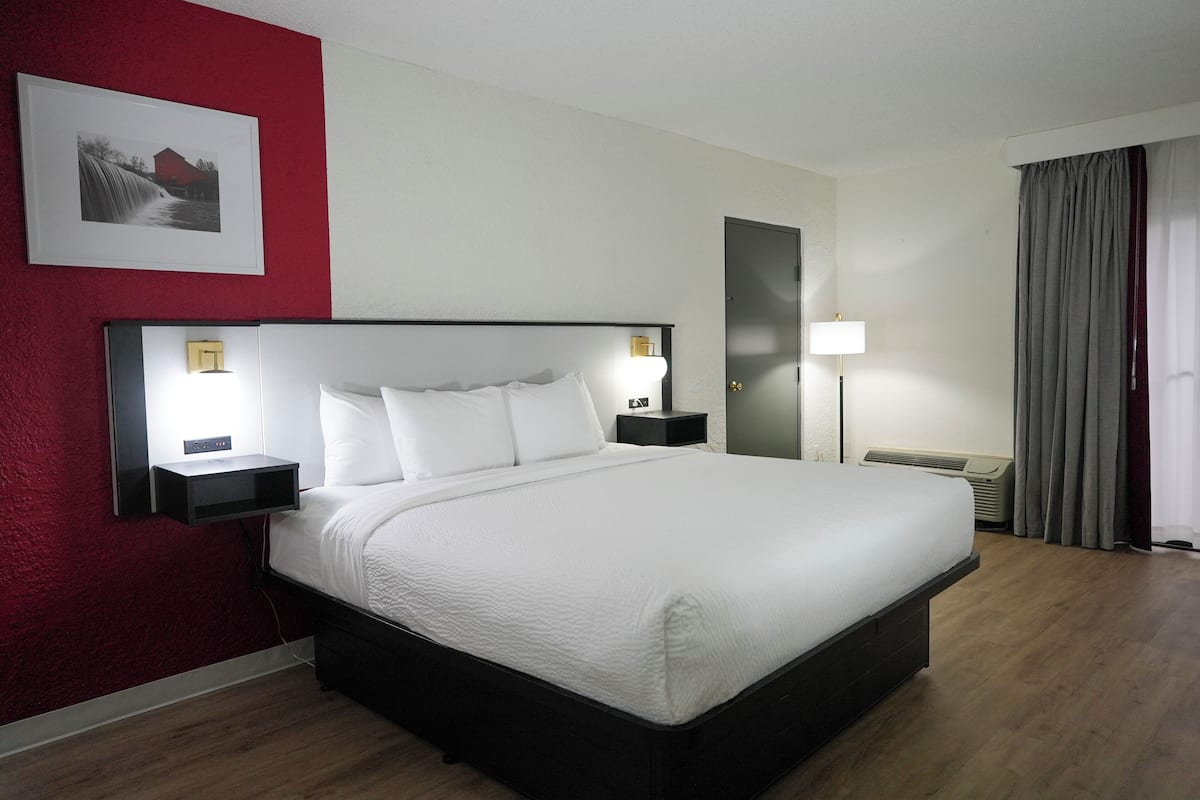 Una habitación de hotel con una cama grande, mesitas de noche con lámparas, una pared de acento roja y un cuadro enmarcado.