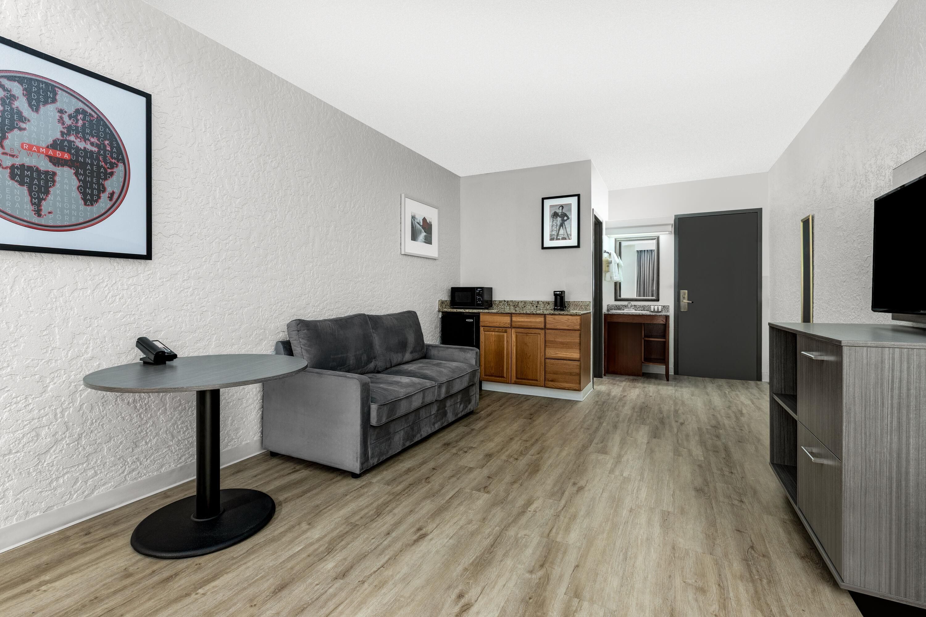 A modern apartment with a grey sofa, a small round table, a kitchen area with wooden cabinets, and a large world map on the wall.