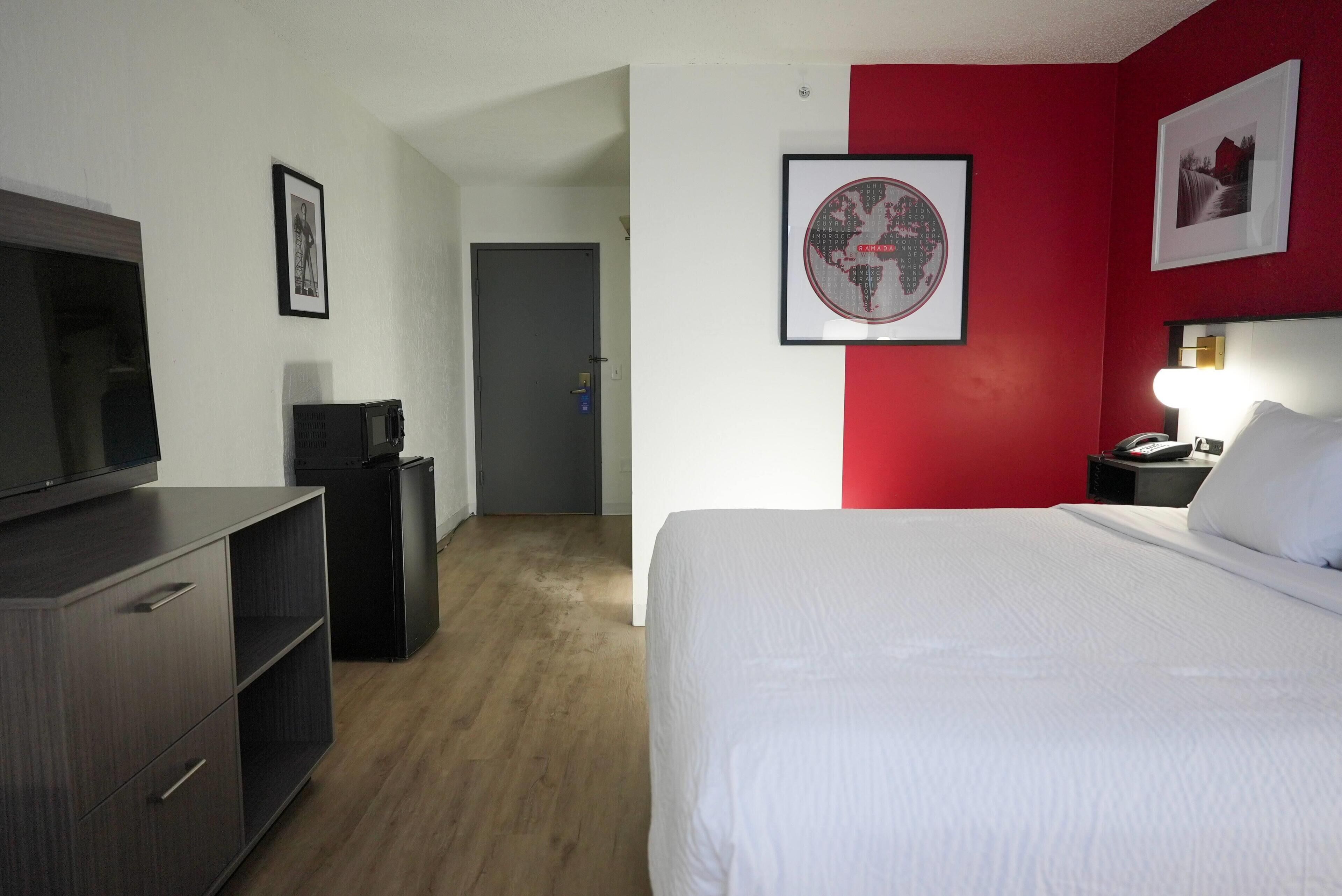 Habitación de hotel con cama, televisión, escritorio y una pared de acento roja.