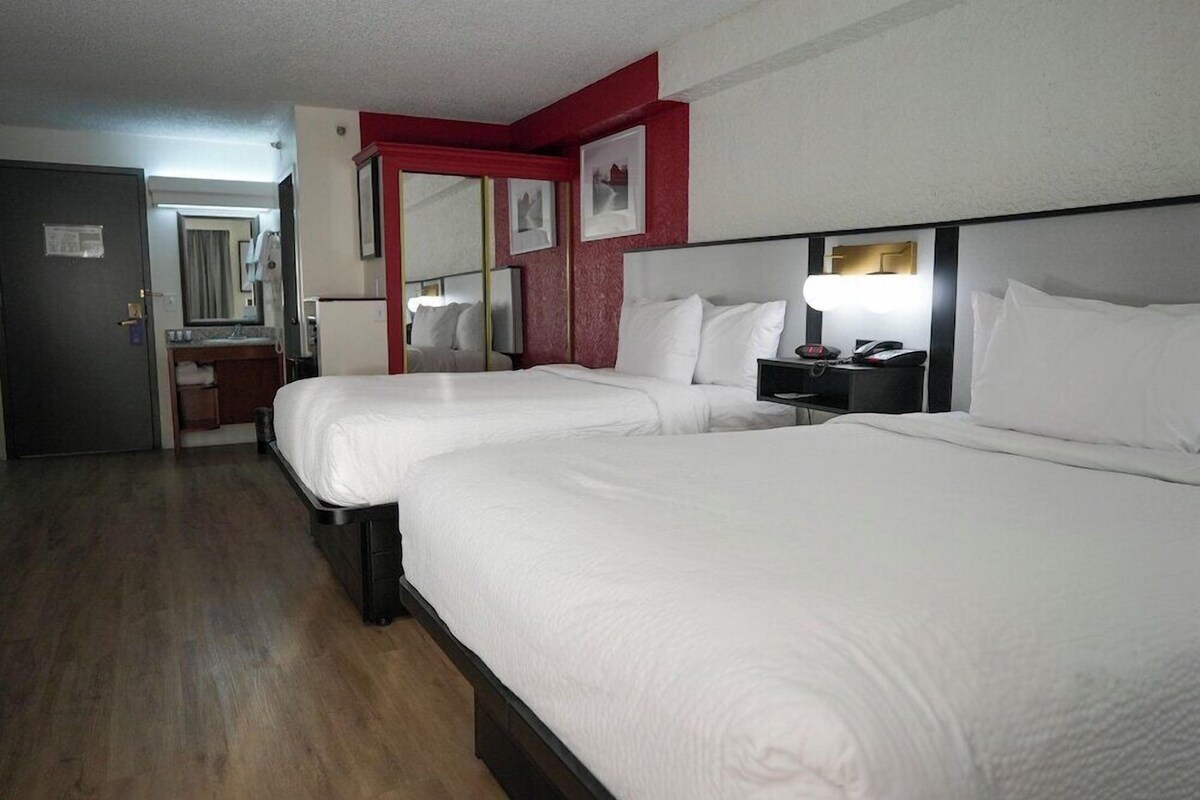 A hotel room with two beds, a bedside table with a lamp, a mirror, and a door to the bathroom.