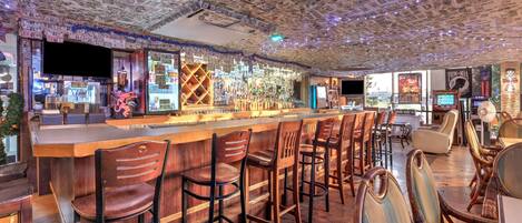 Un bar con techo cubierto de billetes de dólar, taburetes de madera y una variedad de botellas y vasos.