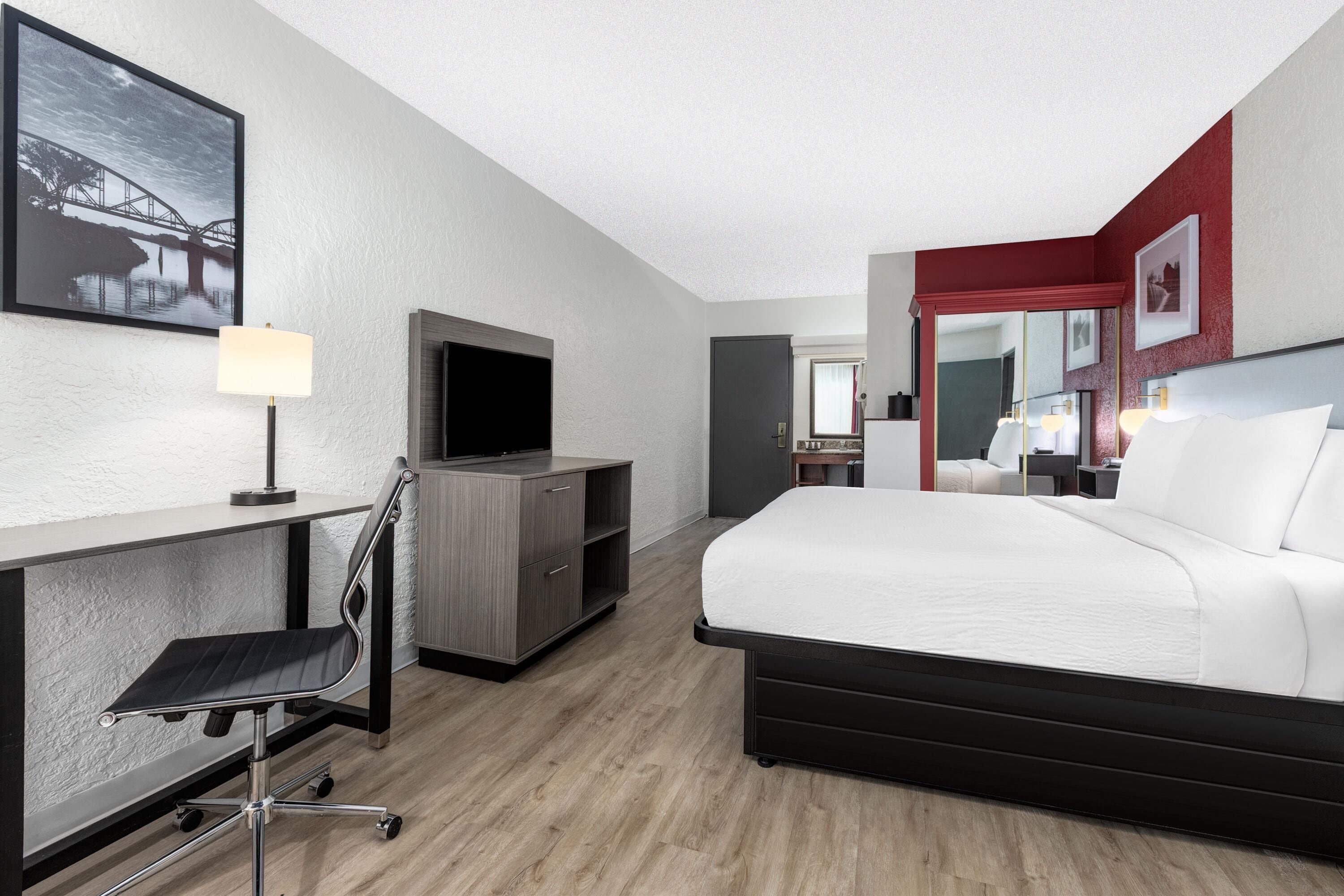 A hotel room with a bed, desk, chair, television, and a mirror.