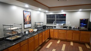 A kitchen with wooden cabinets, a black countertop, and a poster of Tulsa, Oklahoma. - Ramada by Wyndham Tulsa Broken Arrow (Broken Arrow)
