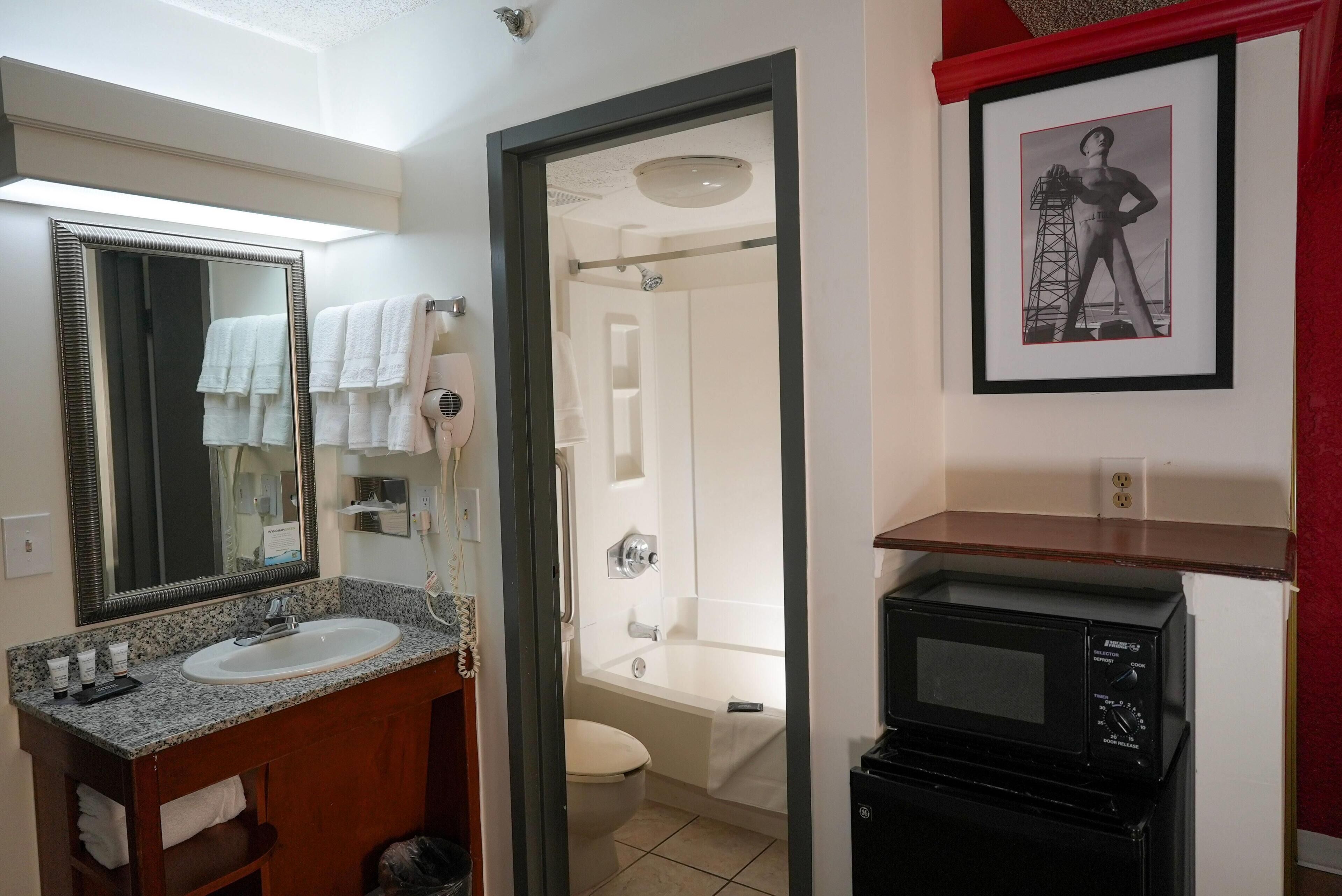 A bathroom with a sink, mirror, towel rack, shower, toilet, and a framed picture on the wall.