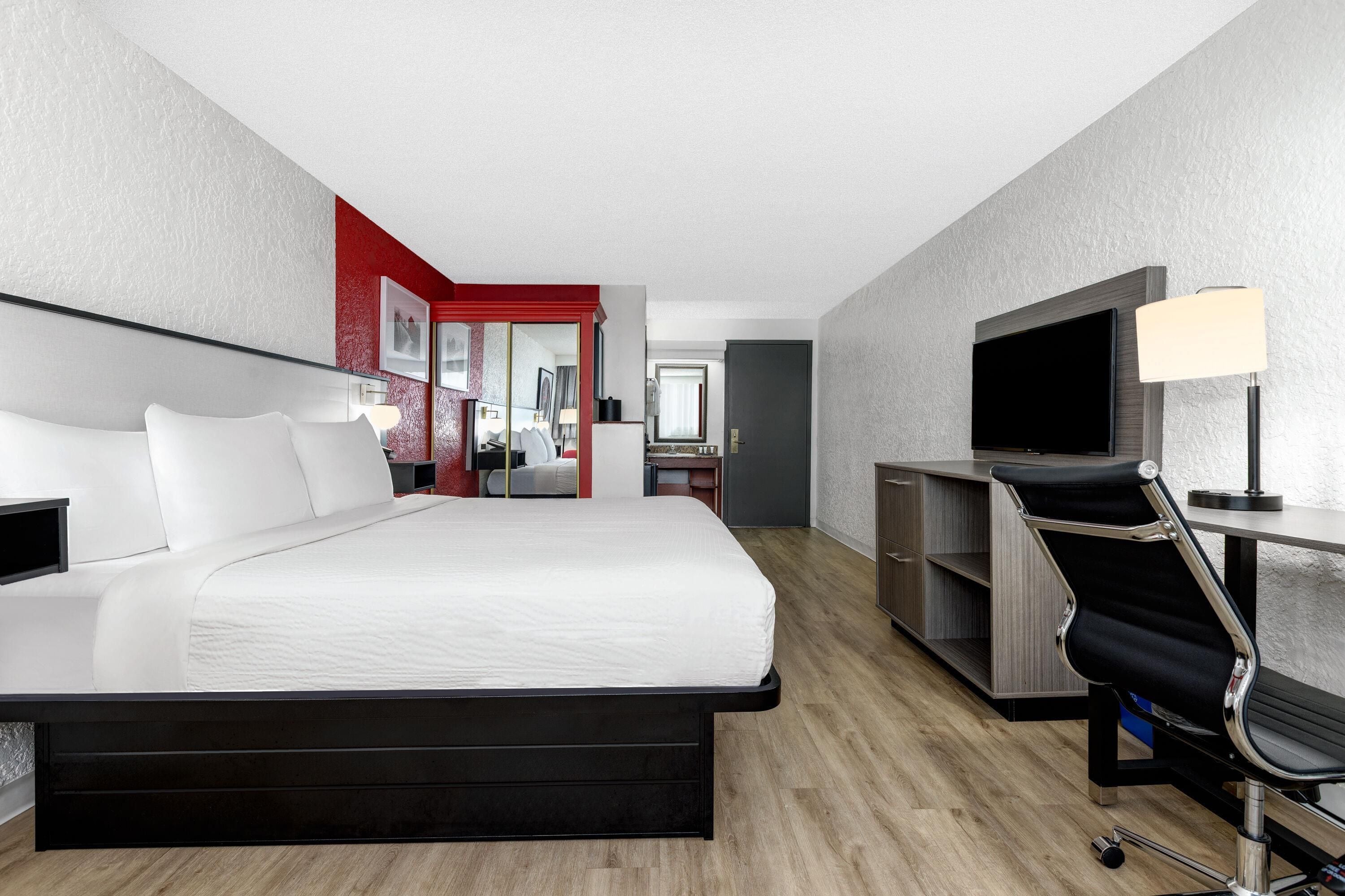 A hotel room with a large bed, a desk with a chair, a TV, and a wardrobe.