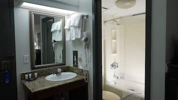 A bathroom with a granite countertop sink, a large mirror, a hairdryer, and a shower with a white towel.