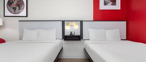 A hotel room with two beds, a nightstand with a phone, and a wall-mounted light fixture.