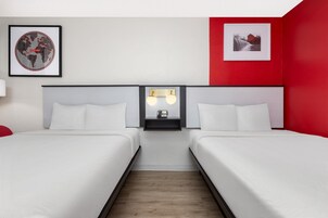 Habitación de hotel con dos camas, una mesita de noche con teléfono y una lámpara de pared.