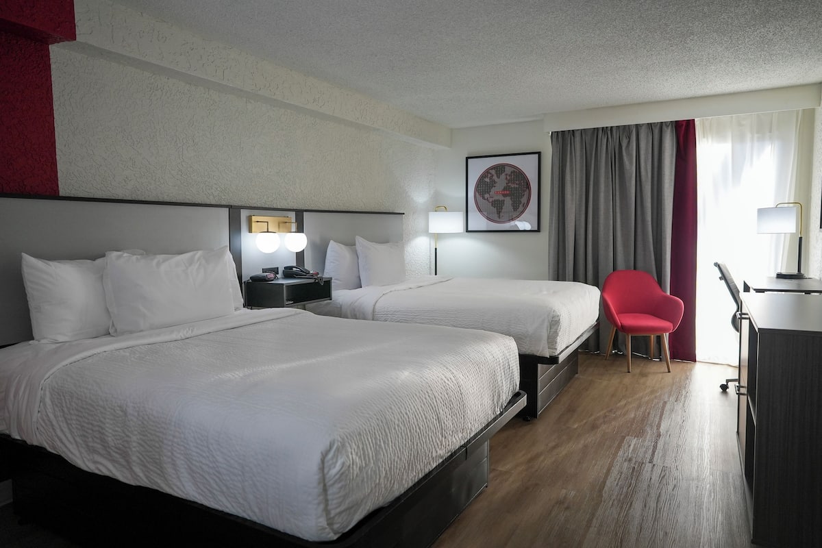 Habitación de hotel con dos camas, un escritorio, una silla y una ventana con cortinas.