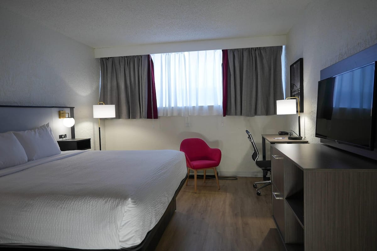 Habitación de hotel con una cama grande, un escritorio con televisor, una silla y una lámpara de escritorio.