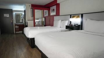 Habitación de hotel con dos camas, un escritorio con lámpara, un espejo y una pared de acento roja.