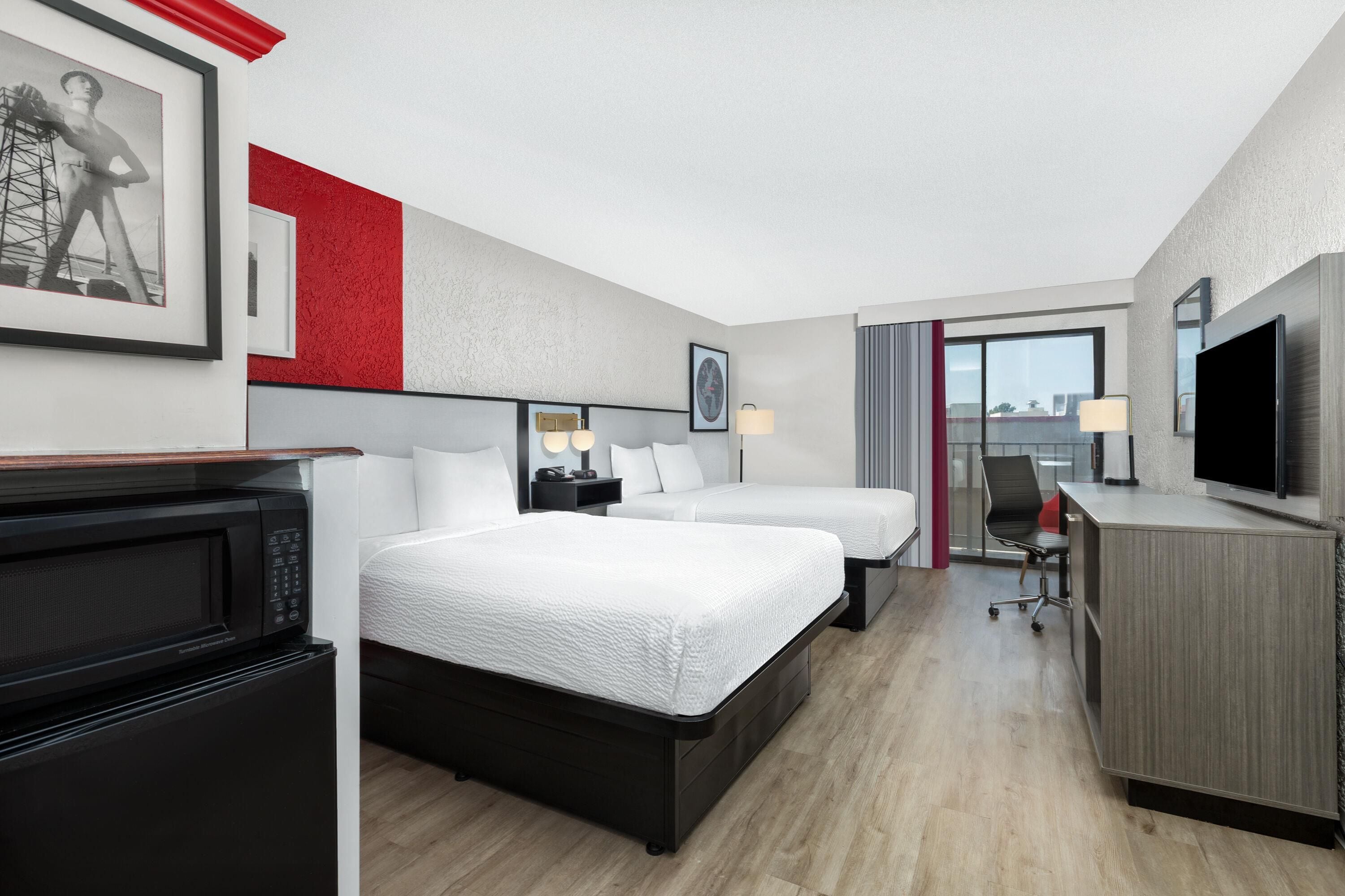 A hotel room with two beds, a desk, a TV, and a microwave.