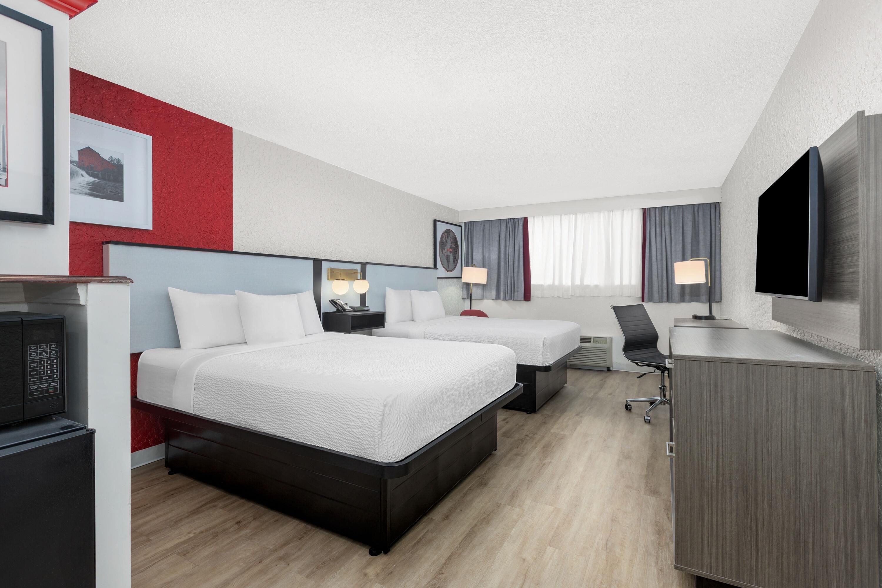 A hotel room with two beds, a desk, a TV, and a minibar.