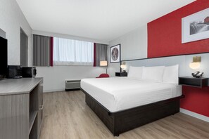 A hotel room with a bed, bedside tables, a desk, a chair, a TV, and a window with curtains. - Ramada by Wyndham Tulsa Broken Arrow (Broken Arrow)