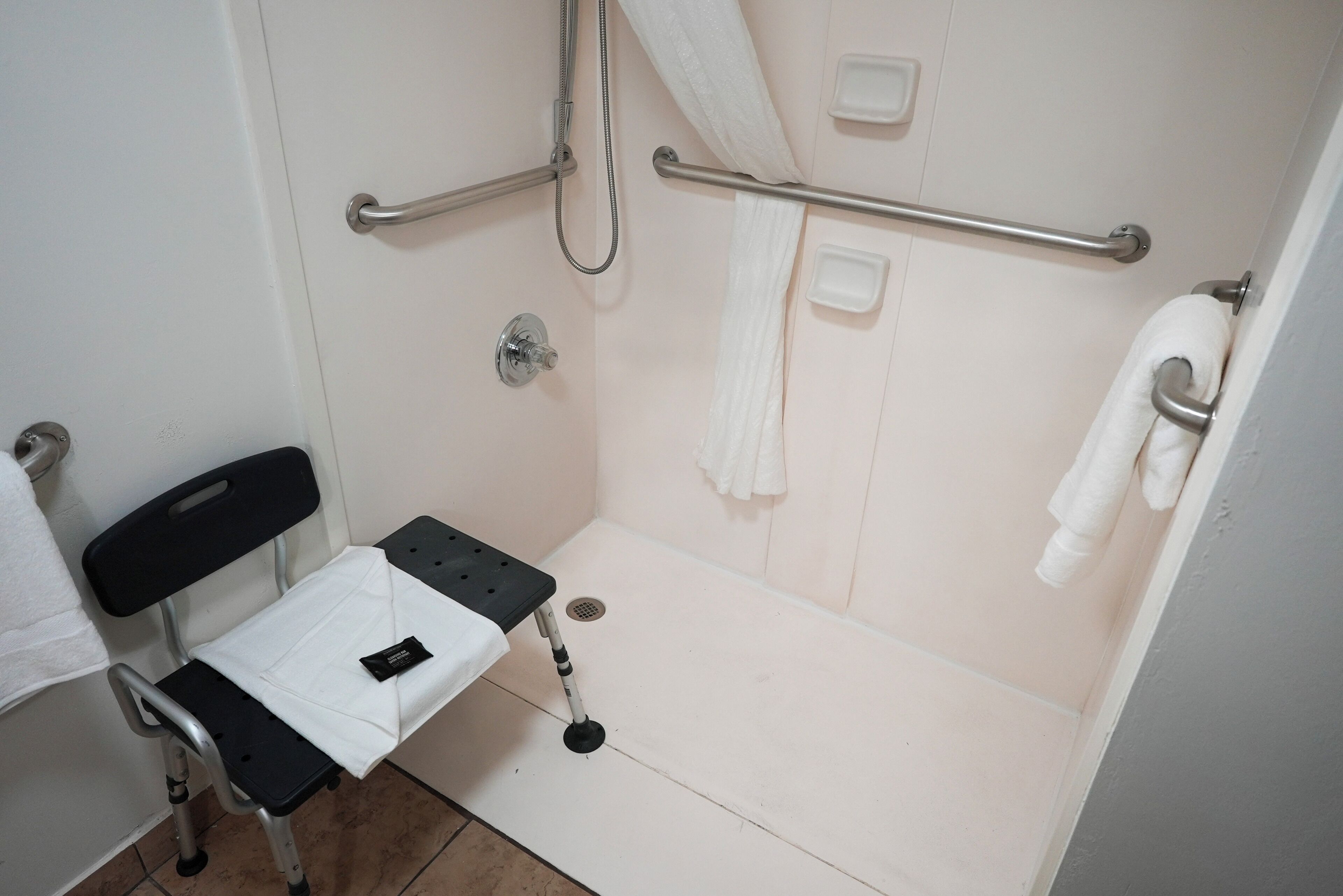 Un baño con ducha, barras de apoyo, una silla de ruedas y un perchero para toallas.