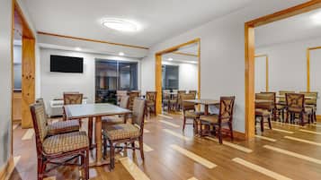 Un'ampia sala da pranzo con diversi tavoli e sedie, un televisore a schermo piatto montato a parete e un grande specchio che riflette l'ambiente.
