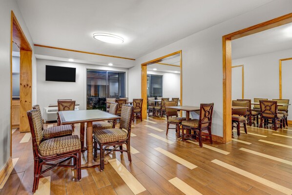 A spacious dining area with multiple tables and chairs, a flat-screen TV mounted on the wall, and a large mirror reflecting the room. - Ramada by Wyndham Tulsa Broken Arrow (Broken Arrow)