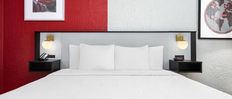 Una habitación de hotel con una cama, dos mesitas de noche, una pared roja y blanca, y dos cuadros enmarcados.