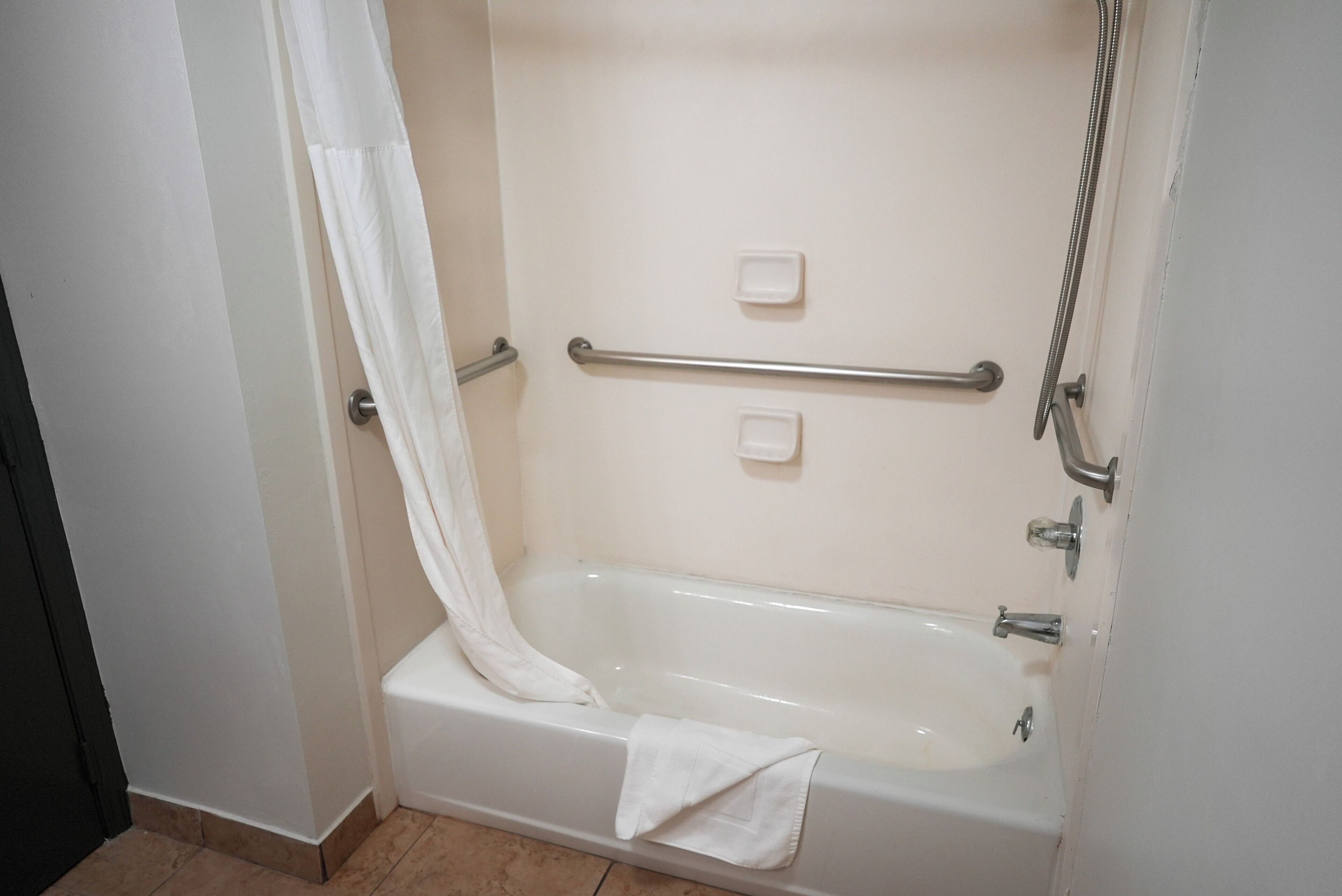 A bathroom with a bathtub, grab bars, and a shower head.