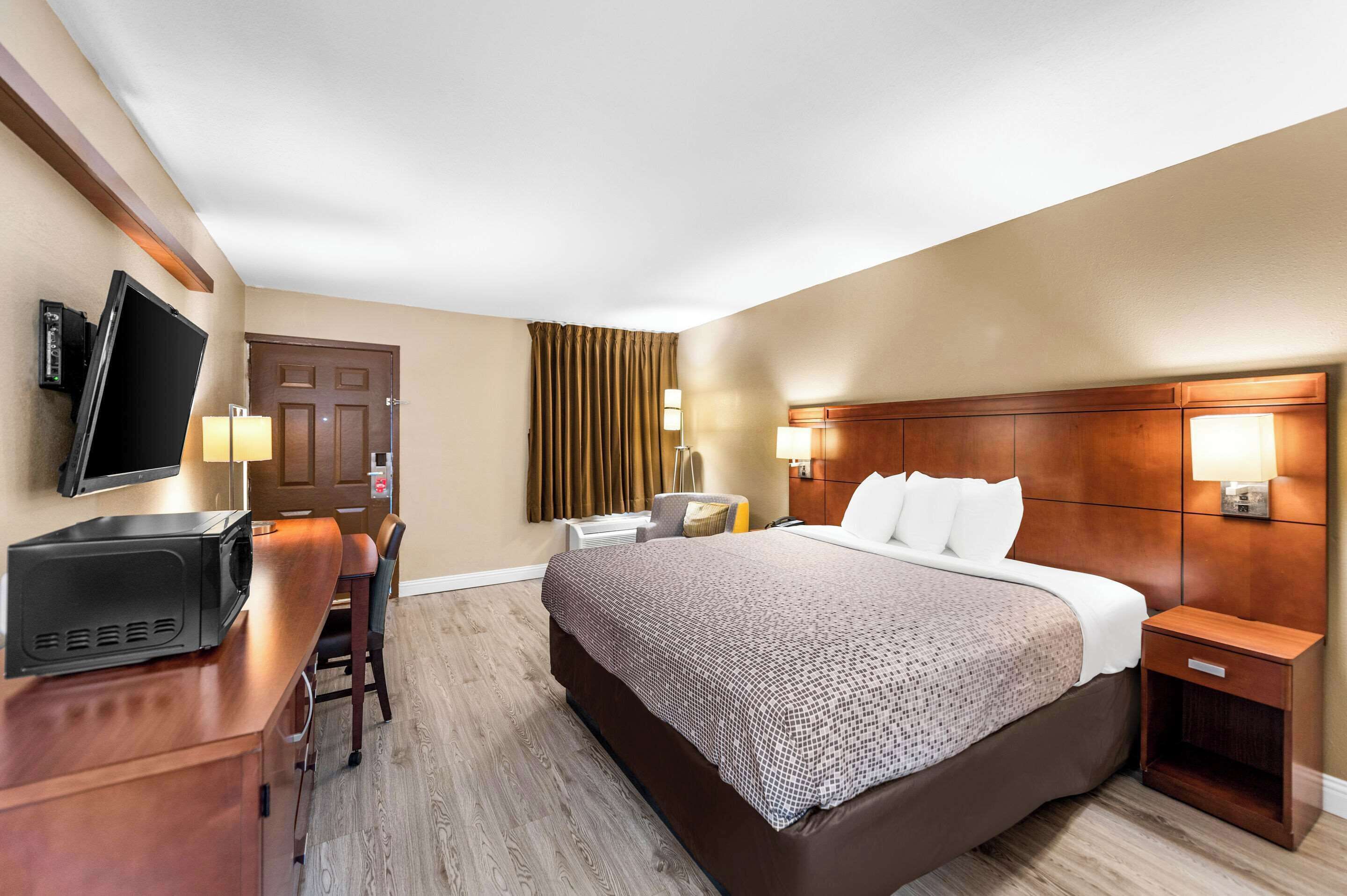 A hotel room with a bed, bedside tables, a desk with a flat-screen TV, and a chair.